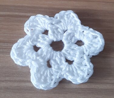 Kleine weiße Häkelblüte mit sechs runden Blütenblättern auf hellem Holz