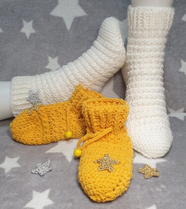Weiße Socken und gelbe gehäkelte Babyschühchen mit Stern-Applikationen auf grauem Sternenstoff
