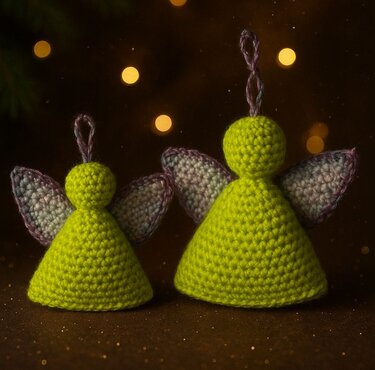 Zwei gehäkelte Amigurumi-Engel in Grün mit violett umrandeten Flügeln vor warmen Lichtern