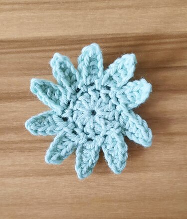 Gehäkelte hellblaue Sternblume auf Holzuntergrund