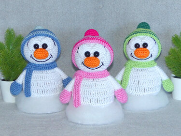 Drei gehäkelte Amigurumi-Schneemänner in Blau, Pink und Grün mit Mützen und Schals