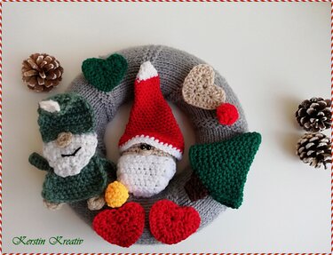 Gehäkelter grauer Weihnachtskranz mit Gnom, Weihnachtsmann, Tannenbaum und Herzen, daneben Tannenzapfen