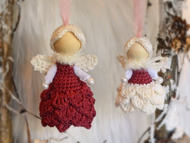 Zwei gehäkelte Amigurumi-Engel in roten und cremefarbenen Kleidern, hängend an Bändern