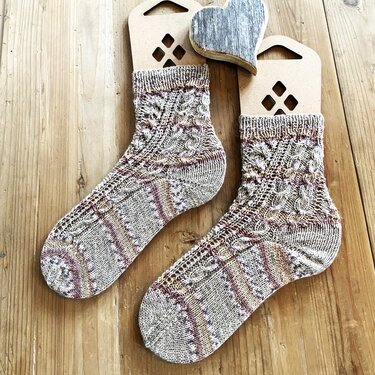 Paar gestrickte Kurzschaft-Socken in Beige- und Lilatönen mit Zopfmuster auf Holzsockenspannern