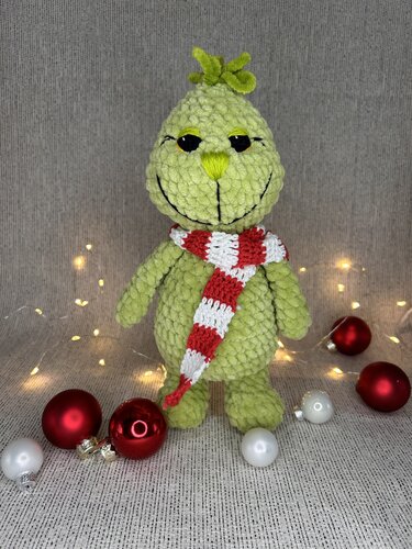 Hellgrünes gehäkeltes Amigurumi mit rot-weißem Schal vor Lichterkette und Weihnachtskugeln