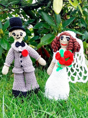 Gehäkeltes Brautpaar Amigurumi: Braut in weißem Kleid mit Schleier und rotem Strauß neben Bräutigam im grauen Anzug mit Zylinder
