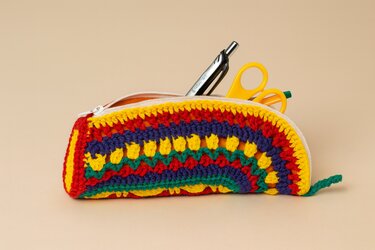 Gehäkeltes Mäppchen in bunten Farben, offen mit Stift und Schere auf beigem Hintergrund