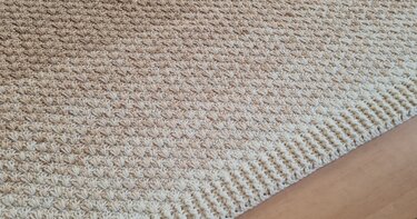 Nahaufnahme einer hellbeigen gehäkelten Decke mit Muschelmuster und gerippter Bordüre.