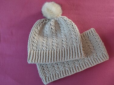 Cremefarbene gestrickte Damenmütze mit Bommel und passendem Stirnband auf rosa Hintergrund