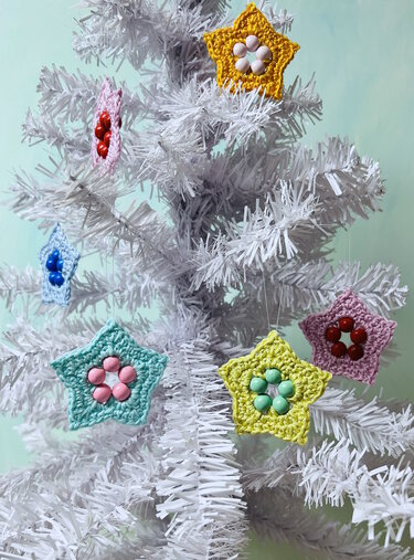 Pastel crochet star ornaments with bead flower centers on a white Christmas tree.