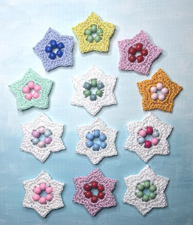 Assorted small crocheted star motifs with beaded centers on a light blue background