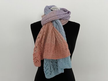 Gestrickter Schal auf schwarzer Schaufensterpuppe in pastelligen Streifen (Rosa, Hellblau, Lila) mit sichtbarem Lochmuster.