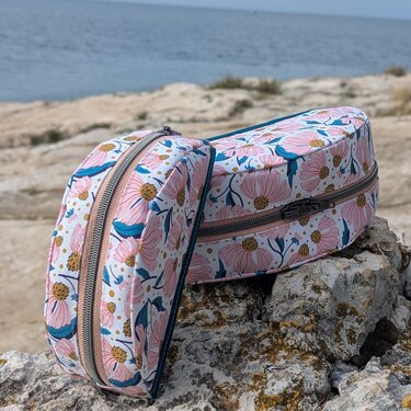 Zwei Kosmetiktaschen mit rosafarbenem Blumenmuster und Reißverschluss auf Felsen am Meer.