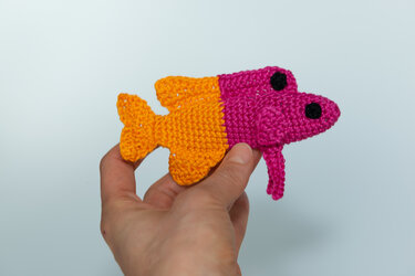 Nahaufnahme eines zweifarbigen gehäkelten Fischs in Pink und Orange mit schwarzen Augen