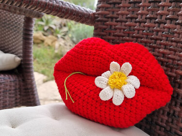 Vivid red lips-shaped crochet cushion decorated with a white daisy on woven seating