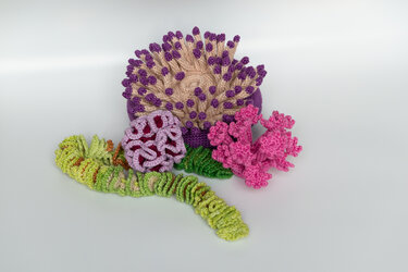 Kleine Amigurumi-Korallen und Seeanemone gehäkelt in Rosa, Violett und Grün auf hellem Hintergrund
