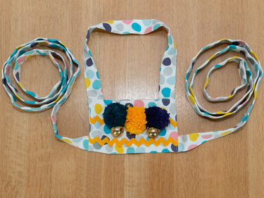 Bunter Musikgürtel mit drei Pompons, zwei Glöckchen und Zackenborte auf Holzboden