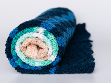 Rolled crocheted baby blanket with blue, mint, white and beige stripes