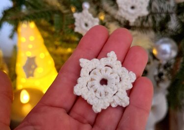 Weiße gehäkelte Schneeflocke in einer Hand vor unscharfer Weihnachtsbeleuchtung