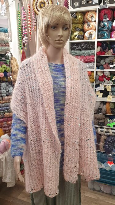 Schaufensterpuppe mit rosa, flauschigem Rechtecktuch mit Pailletten vor Regalen mit Wolle