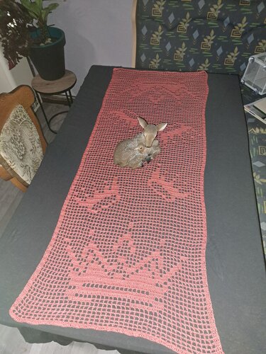 Korallfarbener gehäkelter Filet-Tischläufer mit Kronen- und Tiermotiven auf dunklem Tisch