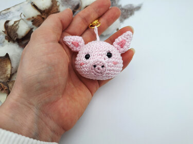 Gehäkeltes rosa Schweinchen mit Öse in Hand, Dekoration im Hintergrund