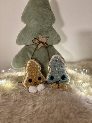 Zwei kleine gehäkelte Amigurumi-Anhänger in Senf und Mint mit Bommelfüßen vor einem Stoffbaum