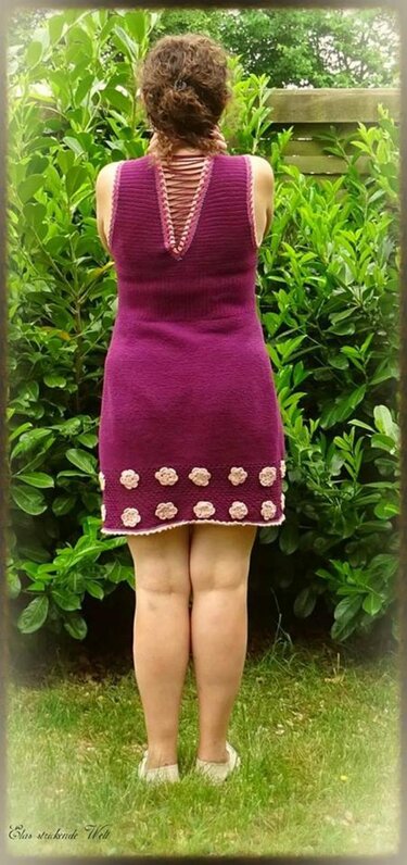 Gehäkeltes pflaumenfarbenes Kleid, Rückenansicht mit geschnürtem V
‑Ausschnitt und hellen Blütenapplikationen am Saum