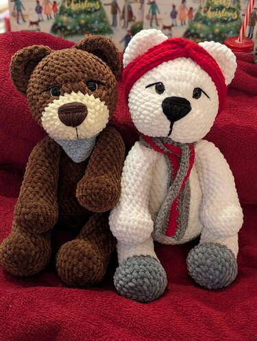 Zwei handgehäkelte Amigurumi-Bären, brauner Teddy und weißer Eisbär mit Schal und Stirnband auf roter Decke.