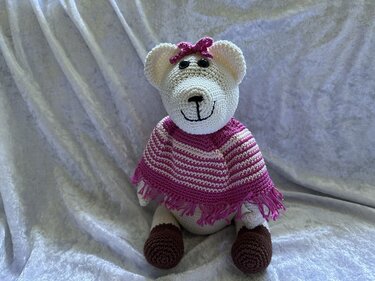 Weißer gehäkelter Teddybär mit pink-weiß gestreiftem Poncho und pinker Schleife