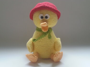 Gelbe Amigurumi-Ente mit rotem Hut und grünem Schal