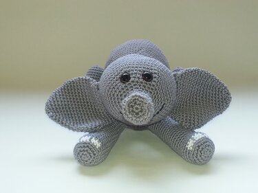 Vorderansicht eines grauen, gehäkelten Elefanten-Amigurumi mit erkennbaren Maschen und dunklen, runden Augen auf hellem Hintergrund.