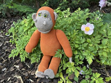 Nahaufnahme eines sitzenden gehäkelten Orang-Utans aus orangegrauem Garn auf Rindenmulch