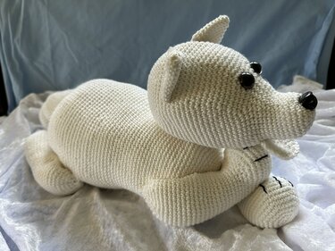 weiß gehäkelter Amigurumi-Bär liegend mit schwarzen Augen und Nase