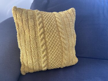 Senfgelbes gestricktes Kissen mit Zopfmuster auf blauem Sofa