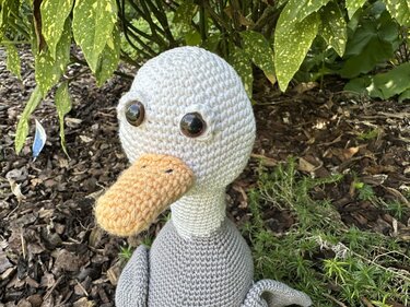 Gehäkelte Ente Amigurumi mit orangenem Schnabel und großen Sicherheitsaugen auf Rindenmulch