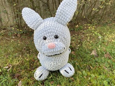 Kuscheliger hellgrauer Amigurumi-Osterhase mit rosa Nase auf Gras