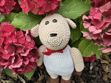 Gehäkeltes Amigurumi-Schaf mit rotem Halstuch zwischen pinken Hortensien
