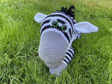 Nahaufnahme eines gestreiften Zebra-Amigurumi mit grauer Schnauze und grünen Sicherheitsaugen