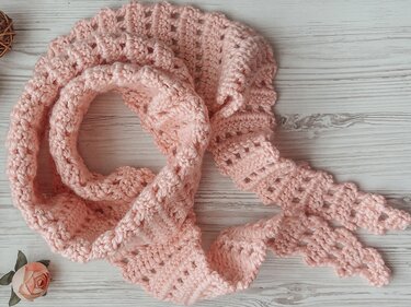 Detailed close-up of a soft pink crochet dragon-tail scarf showing scalloped tail points and open stitch rows