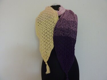 Handgestrickter Dreiecksschal mit Lochmuster und Quasten, Farbverlauf von Gelb über Rosa zu Violett, drapiert an einer Schneiderpuppe.
