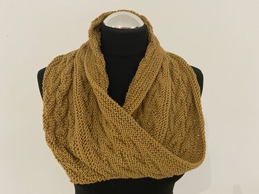 Senfgelber gestrickter Loop-Schal mit Strukturmuster auf schwarzer Schneiderbüste vor hellem Hintergrund.