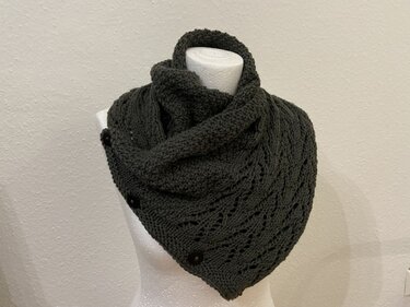 Gestrickter Kragenschal in Dunkelgrau mit Ajourmuster und drei dunklen Knöpfen auf weißer Büste.