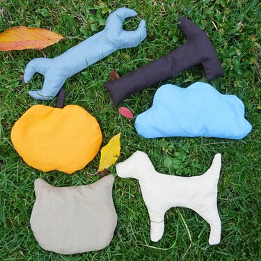 Genähte, gefüllte Stofffiguren (Schraubenschlüssel, Hammer, Wolke, Kürbis, Katzenkopf, Hund) auf Gras