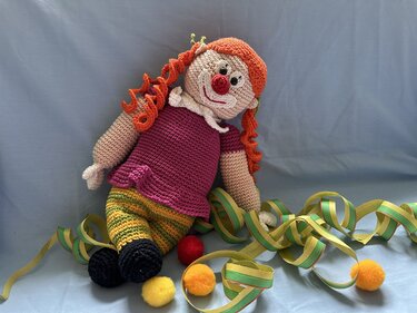 Gehäkelte Clown-Puppe mit orangen Locken, roter Nase, gestreifter Hose, Luftschlangen und Pompons.
