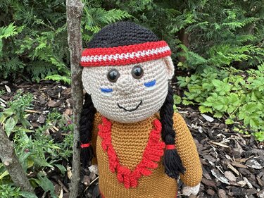 Gehäkelte Amigurumi-Puppe mit schwarzen Zöpfen, rot-weißem Stirnband, braunem Oberteil und rotem Halsschmuck