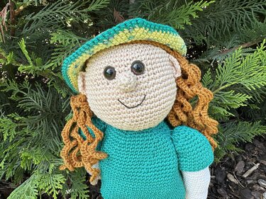 Gehäkelte Amigurumi-Puppe mit großem runden Kopf, Sicherheitsaugen, besticktem Lächeln, lockigen Haaren und gestreiftem Hut