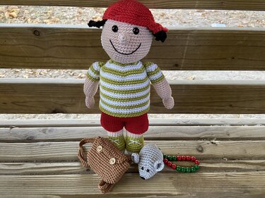 Gehäkelte Amigurumi-Jungenpuppe mit roter Kappe, gestreiftem Shirt, braunem Ranzen und kleiner Maus auf Holzstufen