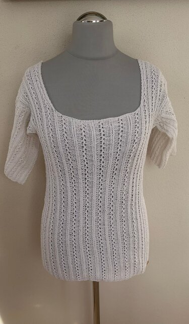 Weißes figurbetontes Strickshirt mit Carré-Ausschnitt und halblangen Ärmeln auf Schneiderpuppe, mit vertikalem Rippen- und Lochmuster.