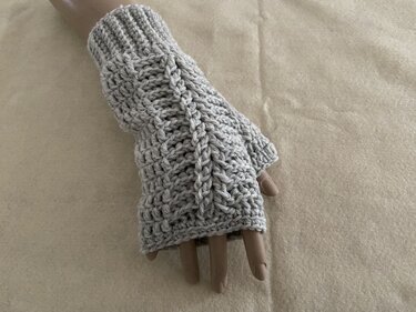 Graue gehäkelte, fingerlose Armstulpe mit Zopfmuster auf Schaufensterpuppenhand